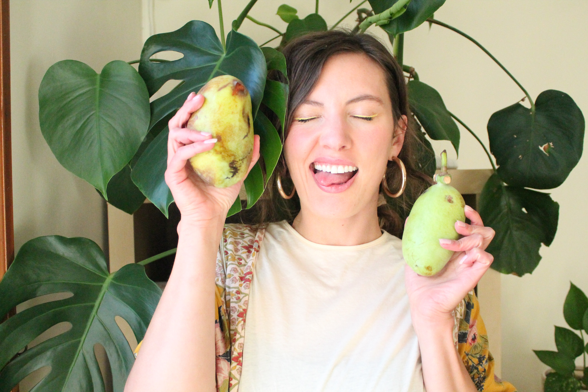 Woman holding pawpaw fruit in front of houseplant