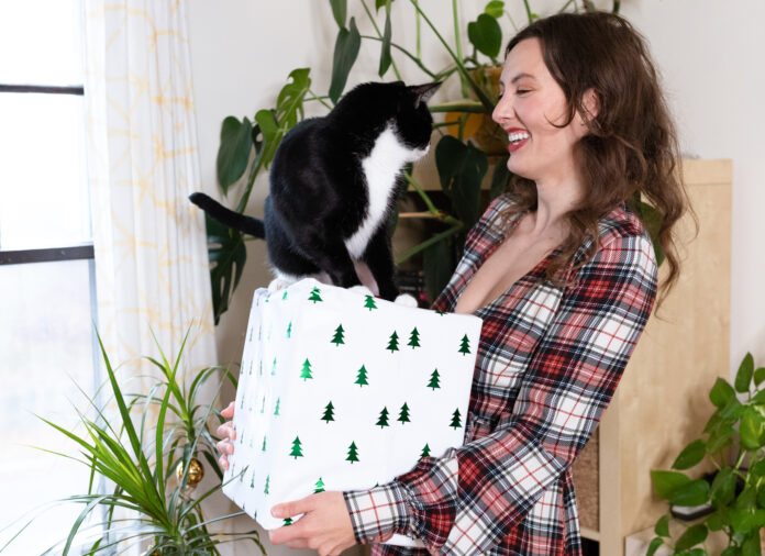 Woman in plaid dress holding holiday gift smiling at cat