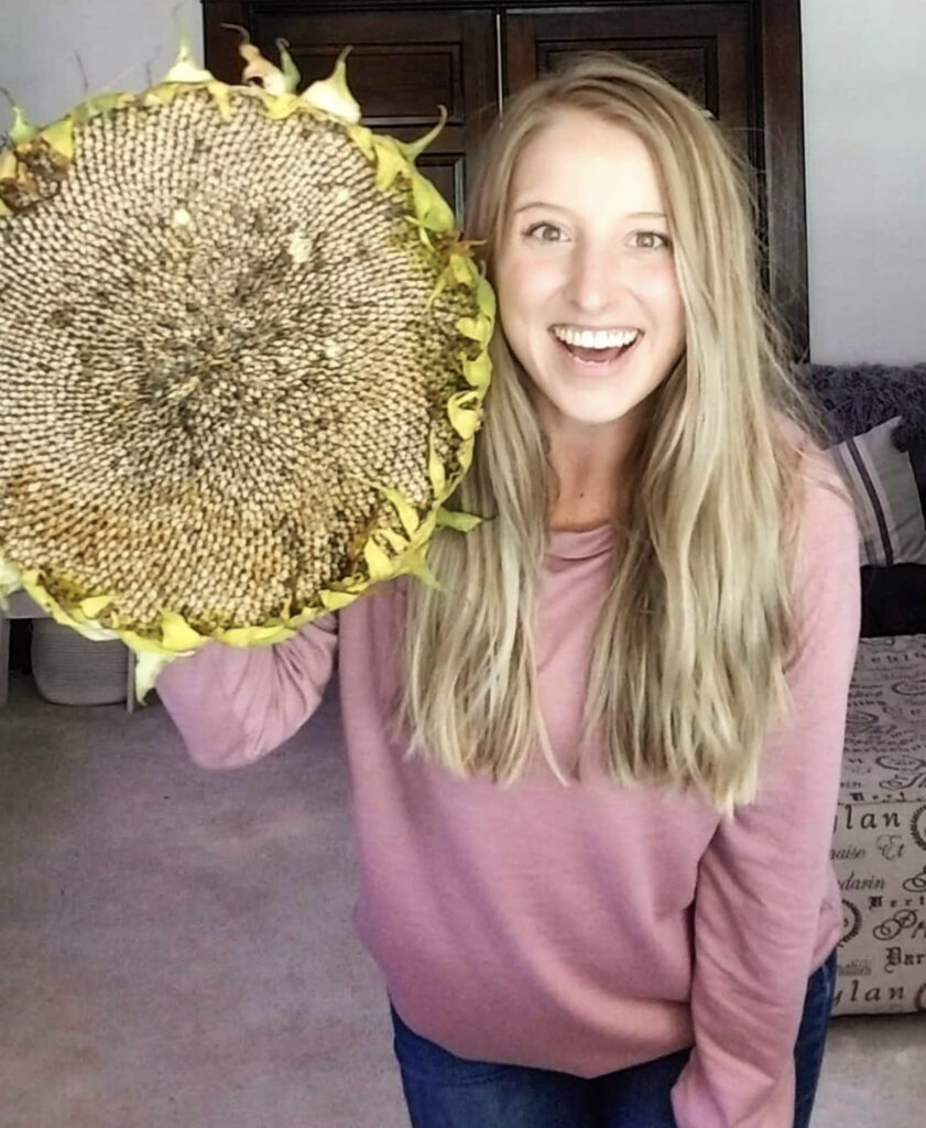 Woman holding up sunflower head next to face and smiling